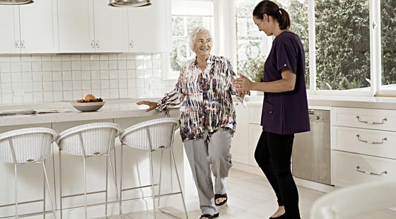 elderly woman and kincare worker lifting their leg up performing exercise in the kitchen