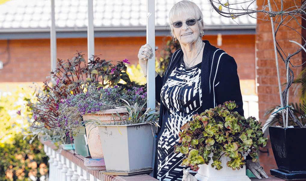 kincare customer maureen smiling amongst her pot plants in her front yard