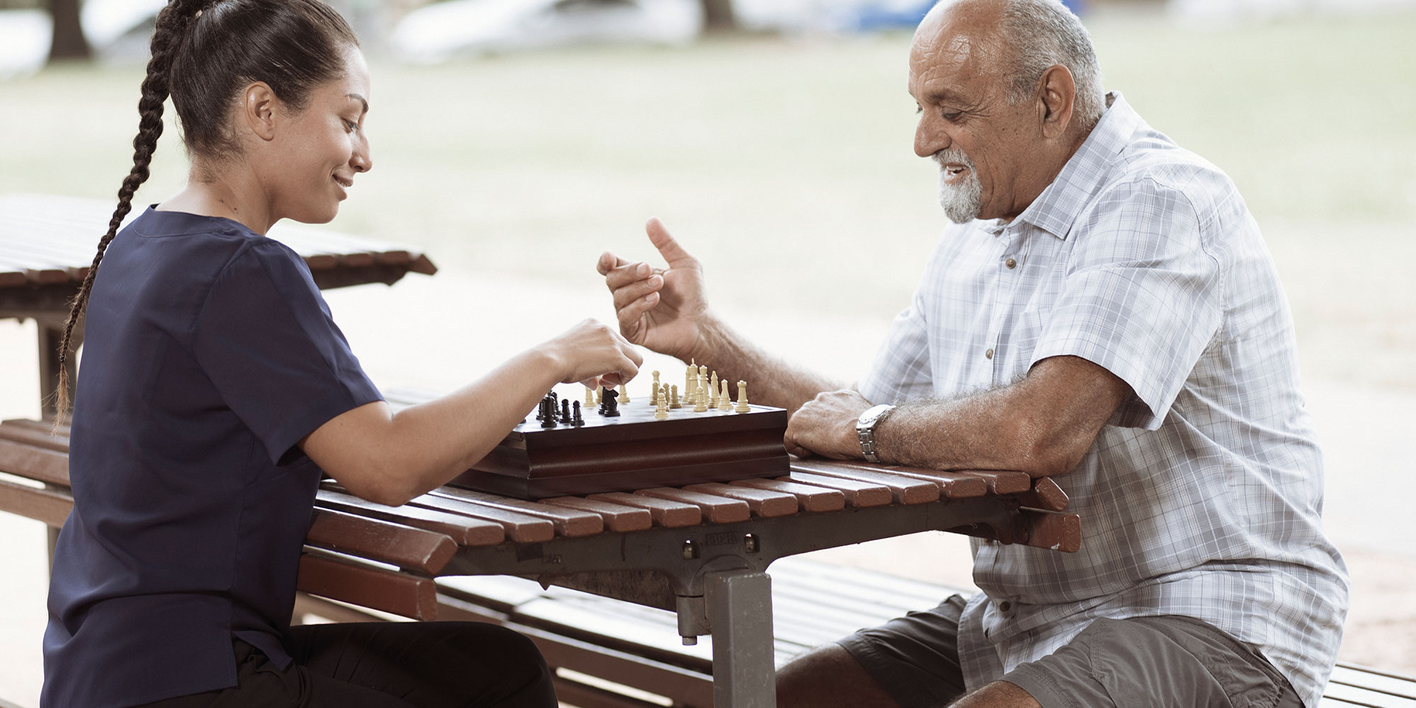 elderly man playing chess outside on a table with kincare worker