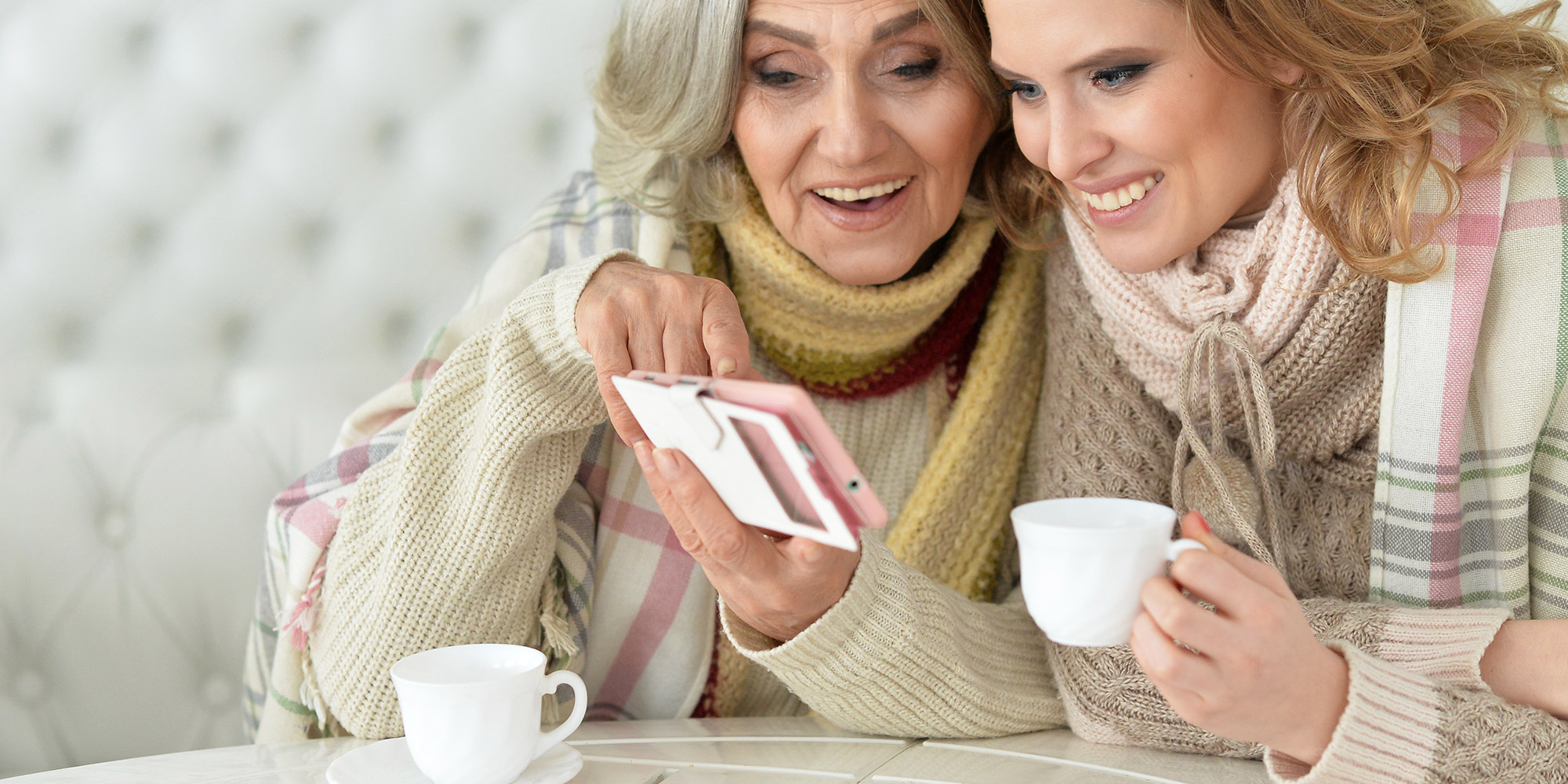 elderly woman showing her phone to a young woman at the coffee table