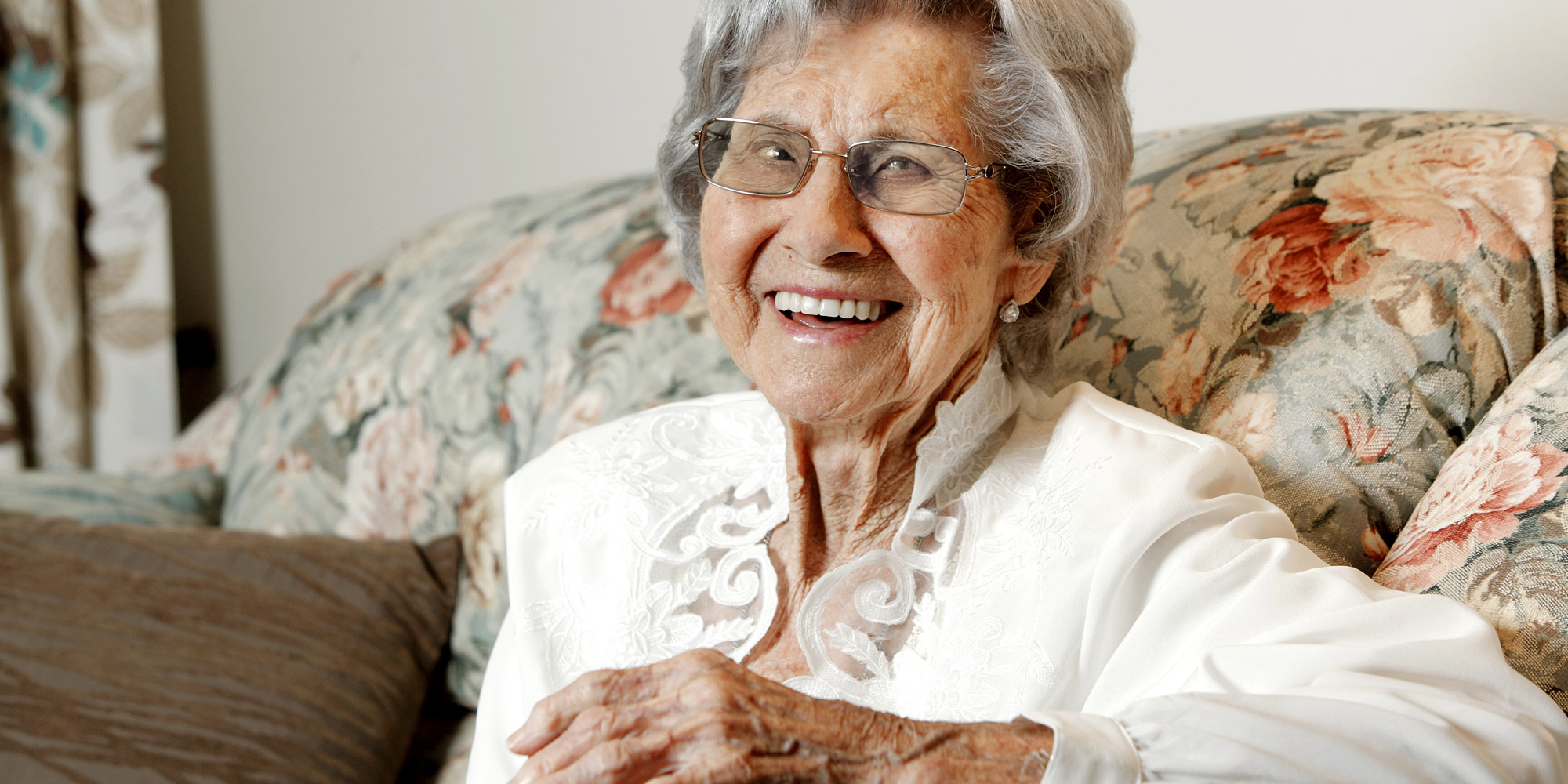 KinCare centenarian, Dorothy Yeomans smiling widely on her floral couch