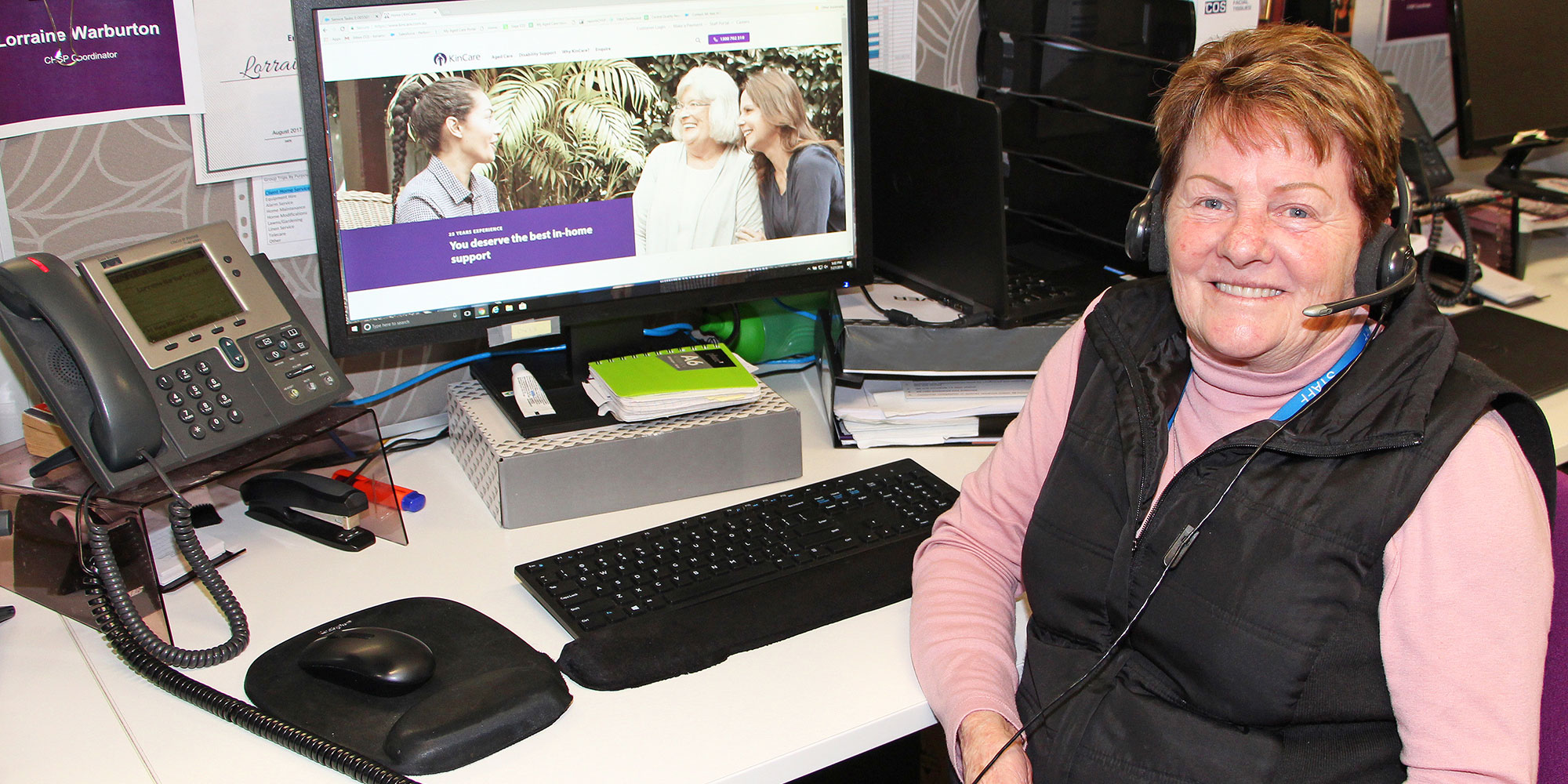 Mature-age KinCare Team memberLorraine sitting at her desk infront of her computer with a headset on