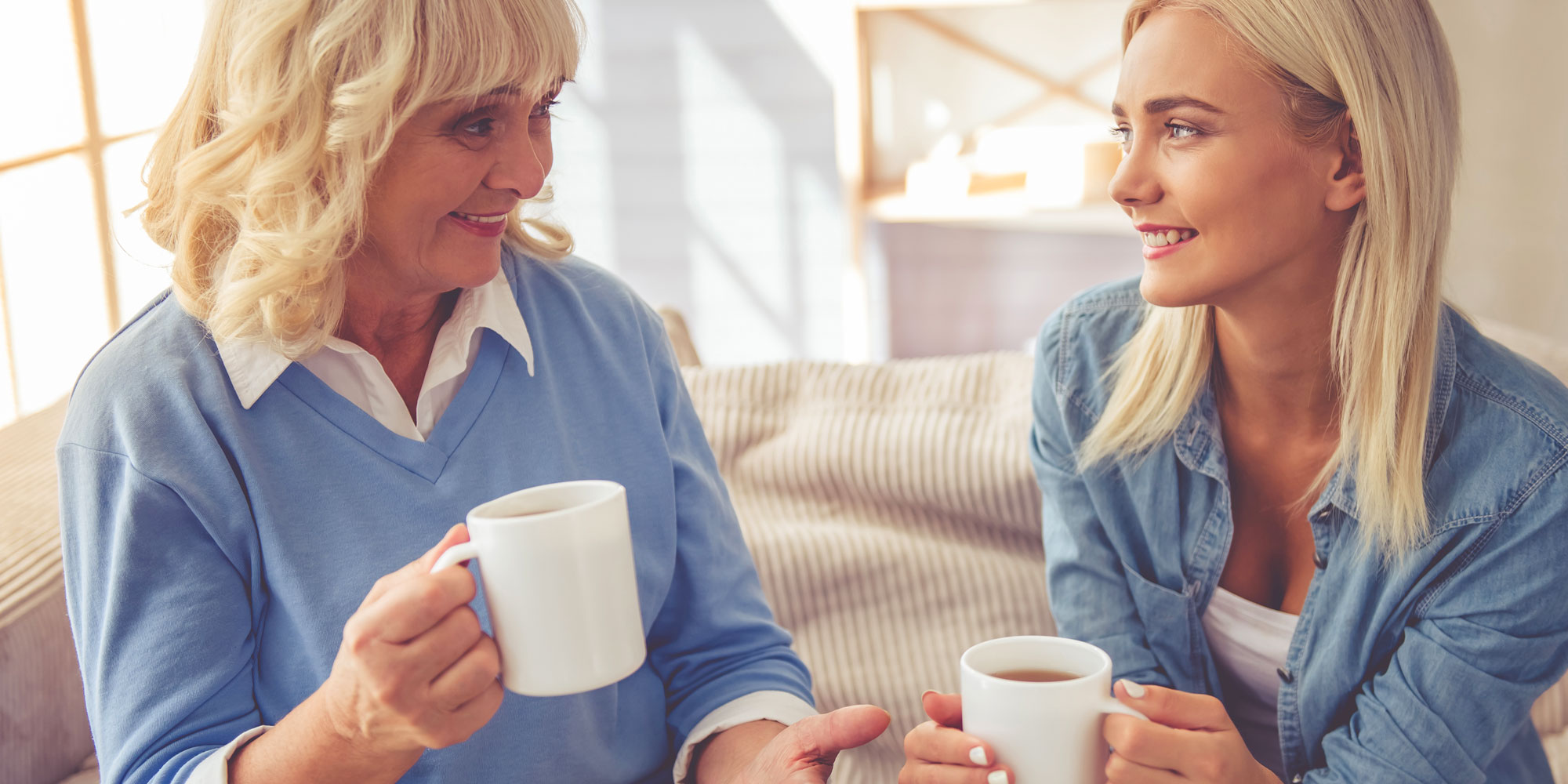 elderly woman and young lady each holding a cup of tea smiling to eachother