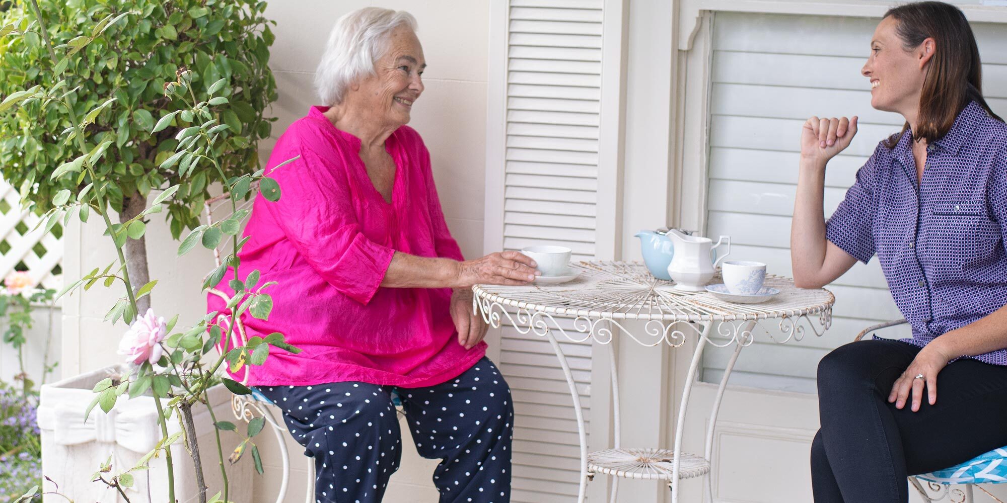 Elderly woman and kincare worker drinking tea together whilst sitting outdoors