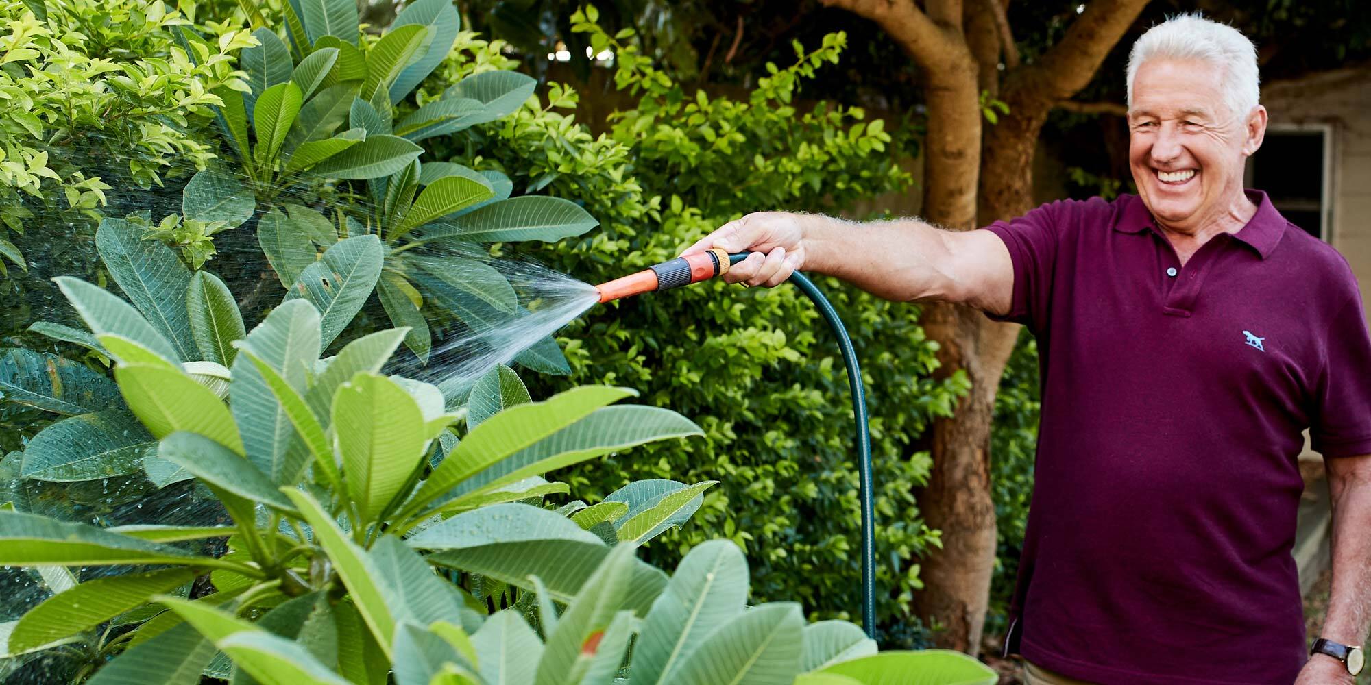 elderly man watering pants with a hose in the garden and smiling