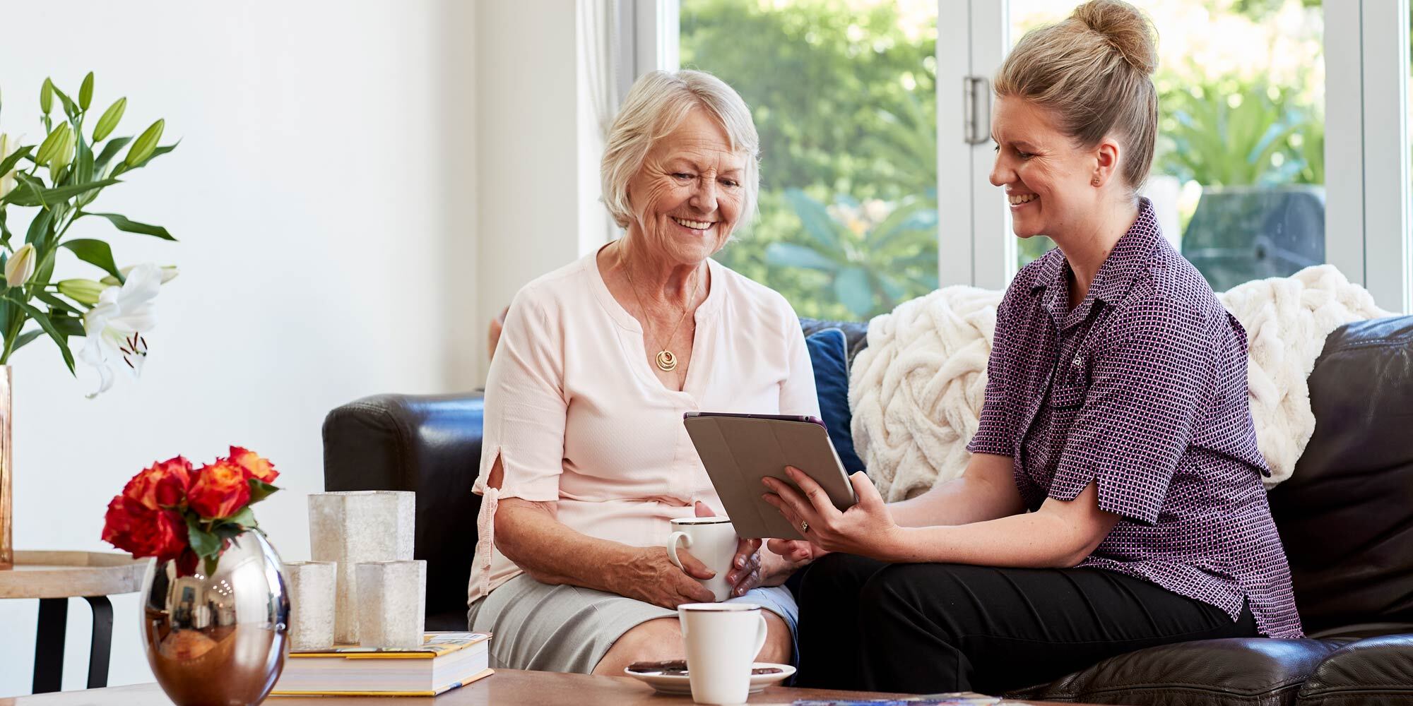 A KinCare home care shows an older woman how to use a tablet.