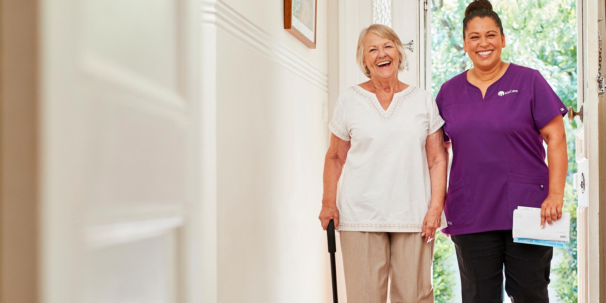Kincare worker assisting elderly woman with walking stick smiling and walking together