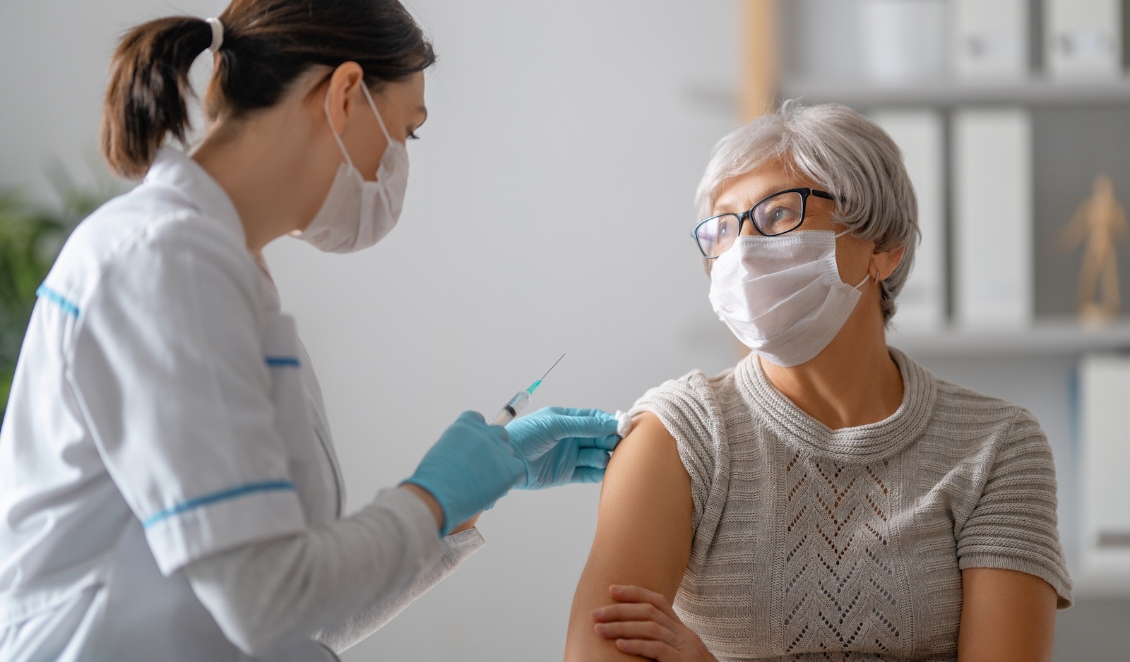 Nurse vaccinating elderly woman with covid-19 vaccine wearings masks