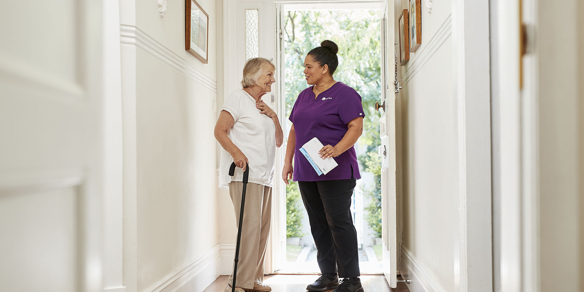 Elderly woman with walking stick smiling and talking to Kincare worker