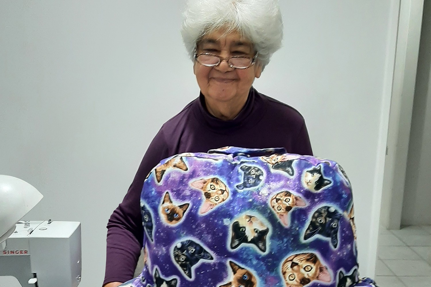 Customer Rosanna smiling next to sewing machine and a purple pillow with patterned cat faces