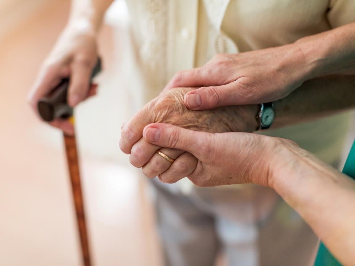 A close-up of an elderly hand, held gently by two younger hands.