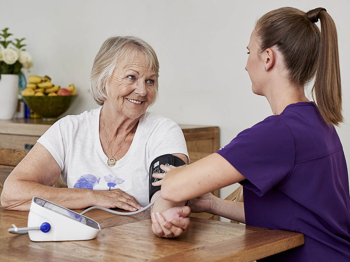 A lady having her blood pressure taken by her KinCare Nurse at the dining table.